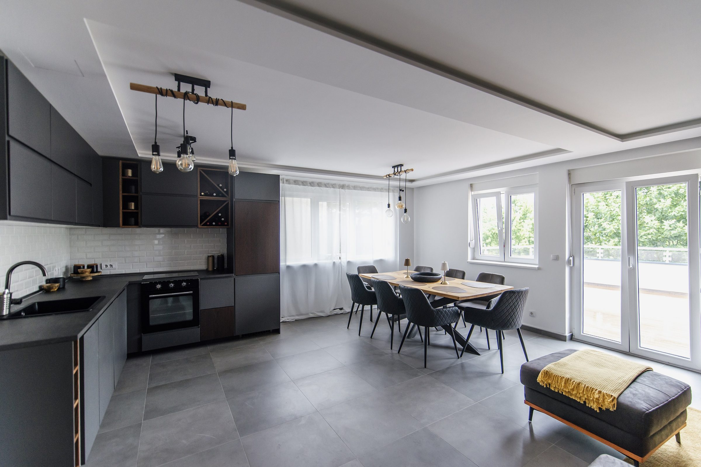 The open main volume: dark kitchen along one wall, the long table under tall windows